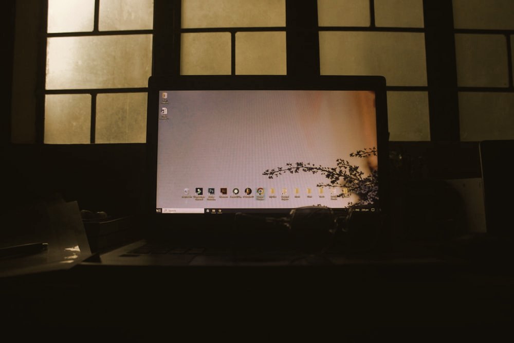 A laptop glowing in a dark room beside a window