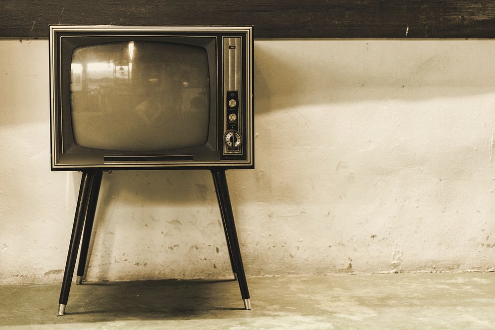 A vintage CRT television on splayed legs against a weathered wall